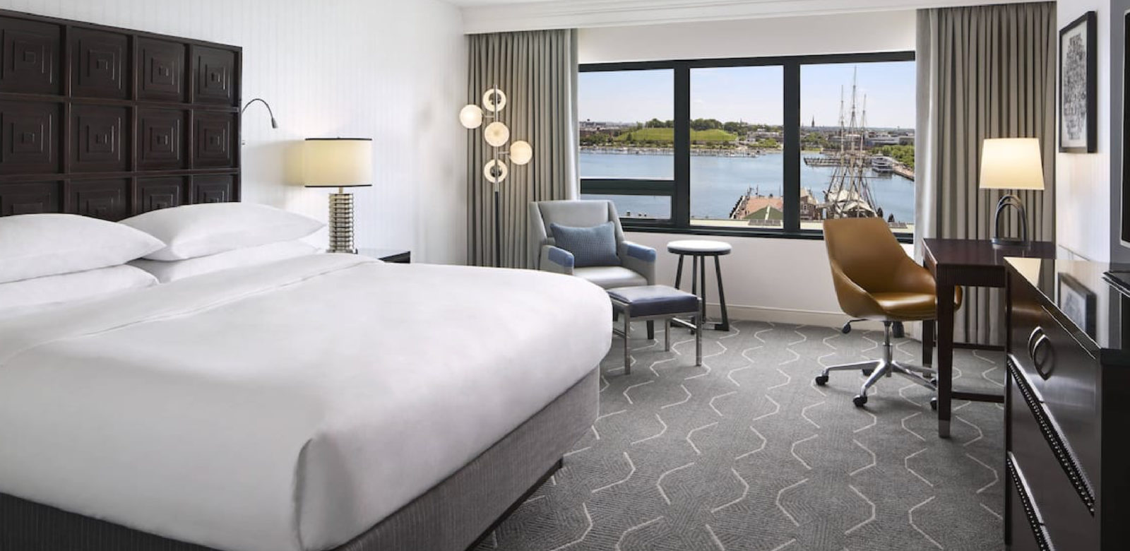 Room with bed, desk, and seating are with view of harbor