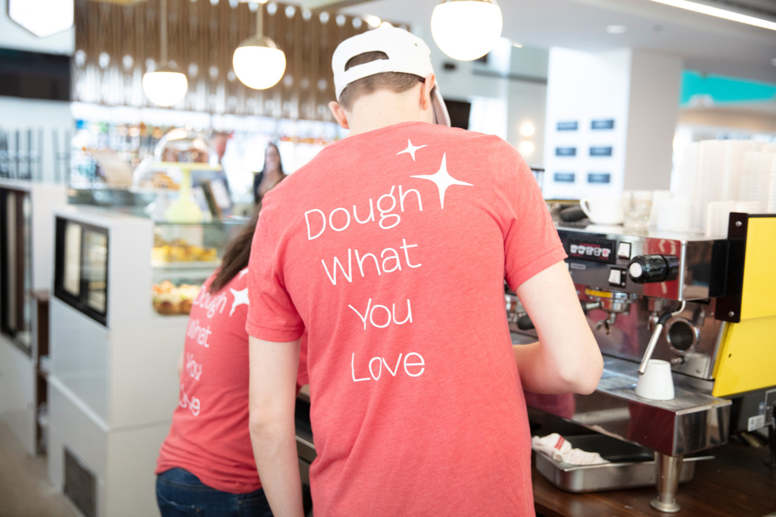 Associates making coffee at Spark'd with shirts that say "Dough what you love"