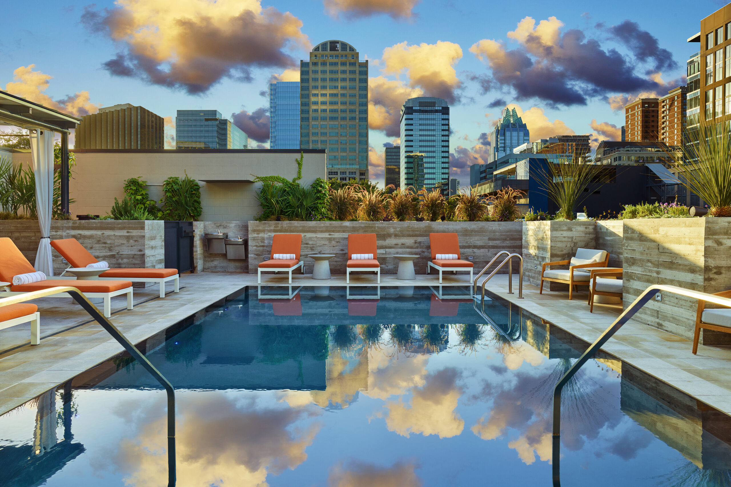 Image of pool and orange lounge chairs at Canopy Austin with Austin skyline in the background